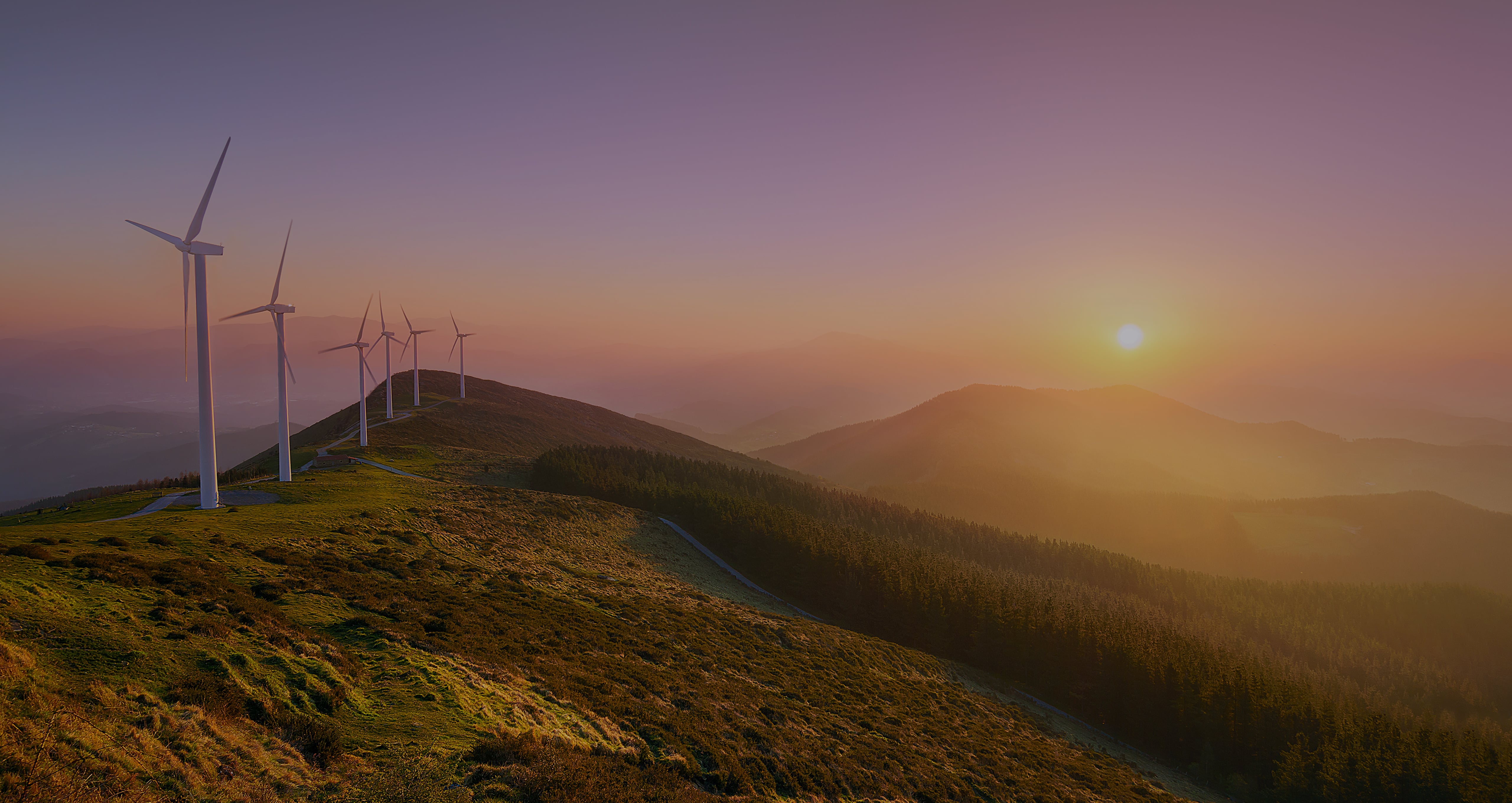 A panoramic image featuring wind turbines on a hill at sunrise on the left, transitioning to a bright sun setting over a landscape on the right, illustrating the focus on renewable energy and sustainable growth.