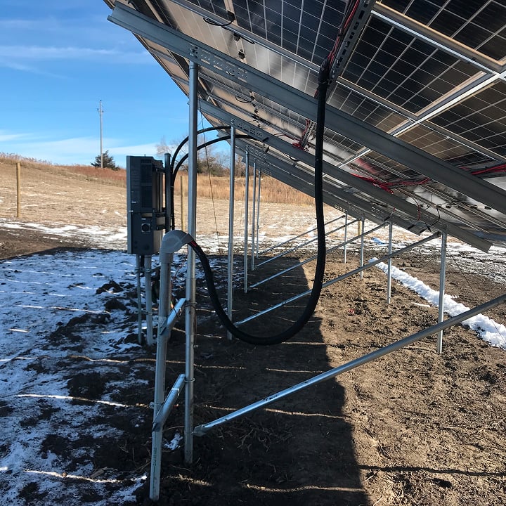 A ground-mounted solar panel array is visible in a snowy, rural landscape under a clear blue sky.